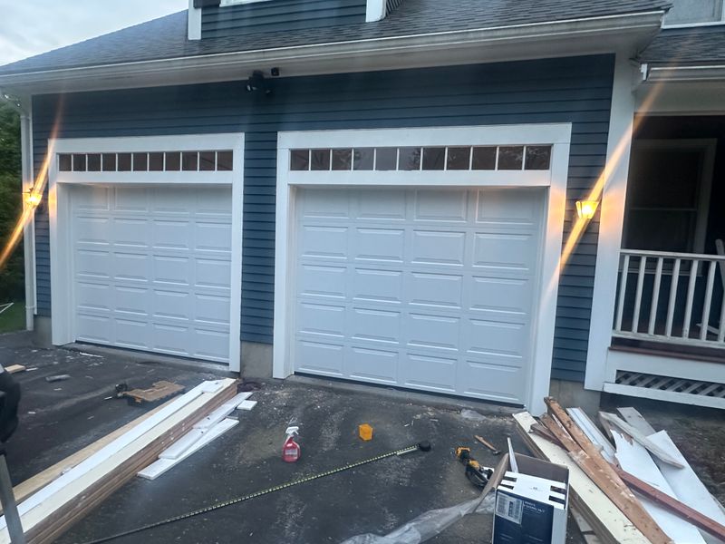 Completed dual white garage doors with transom windows on blue colonial at dusk — MA