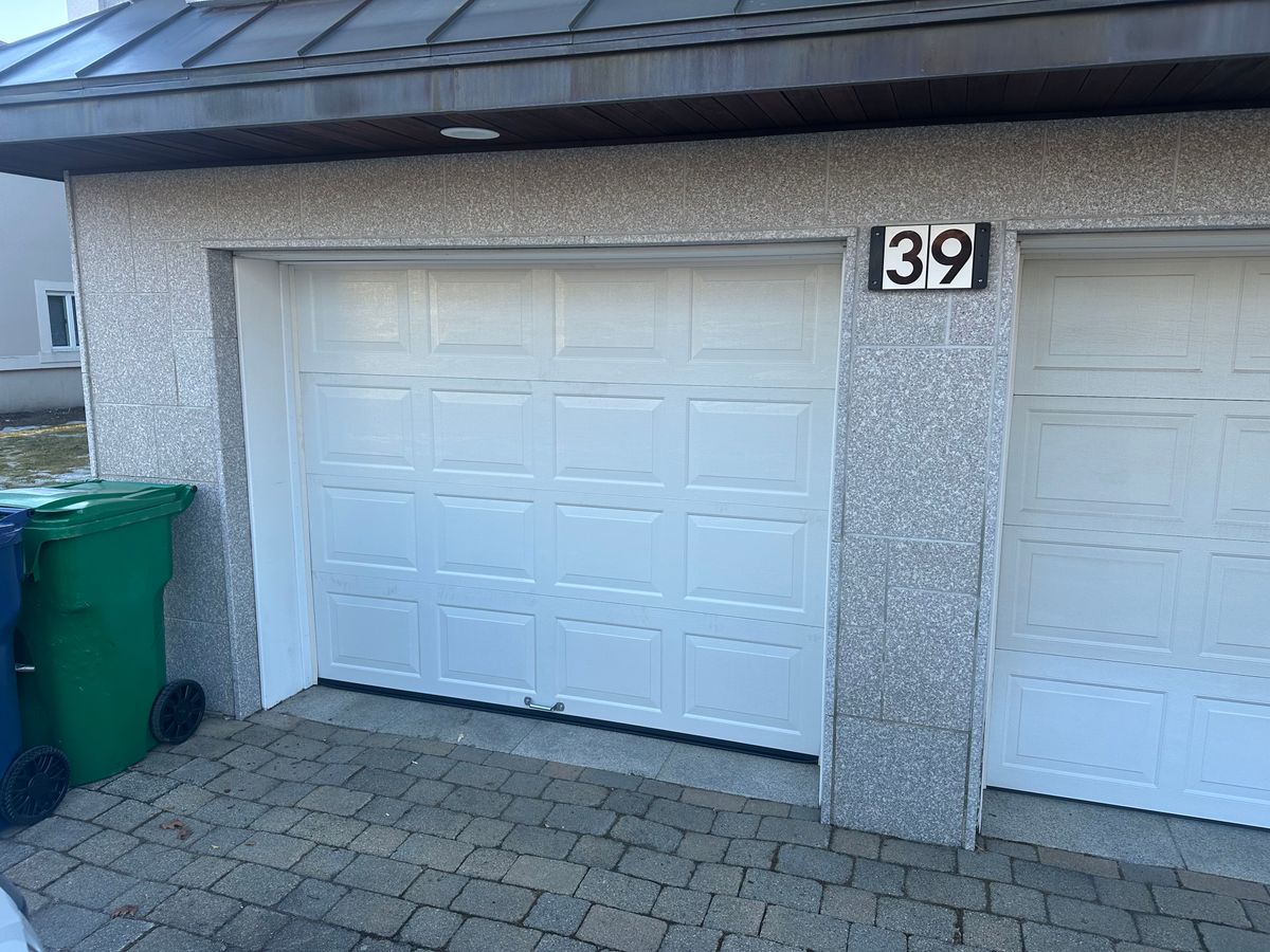 Older white raised-panel garage door before replacement on stone-faced home in MA